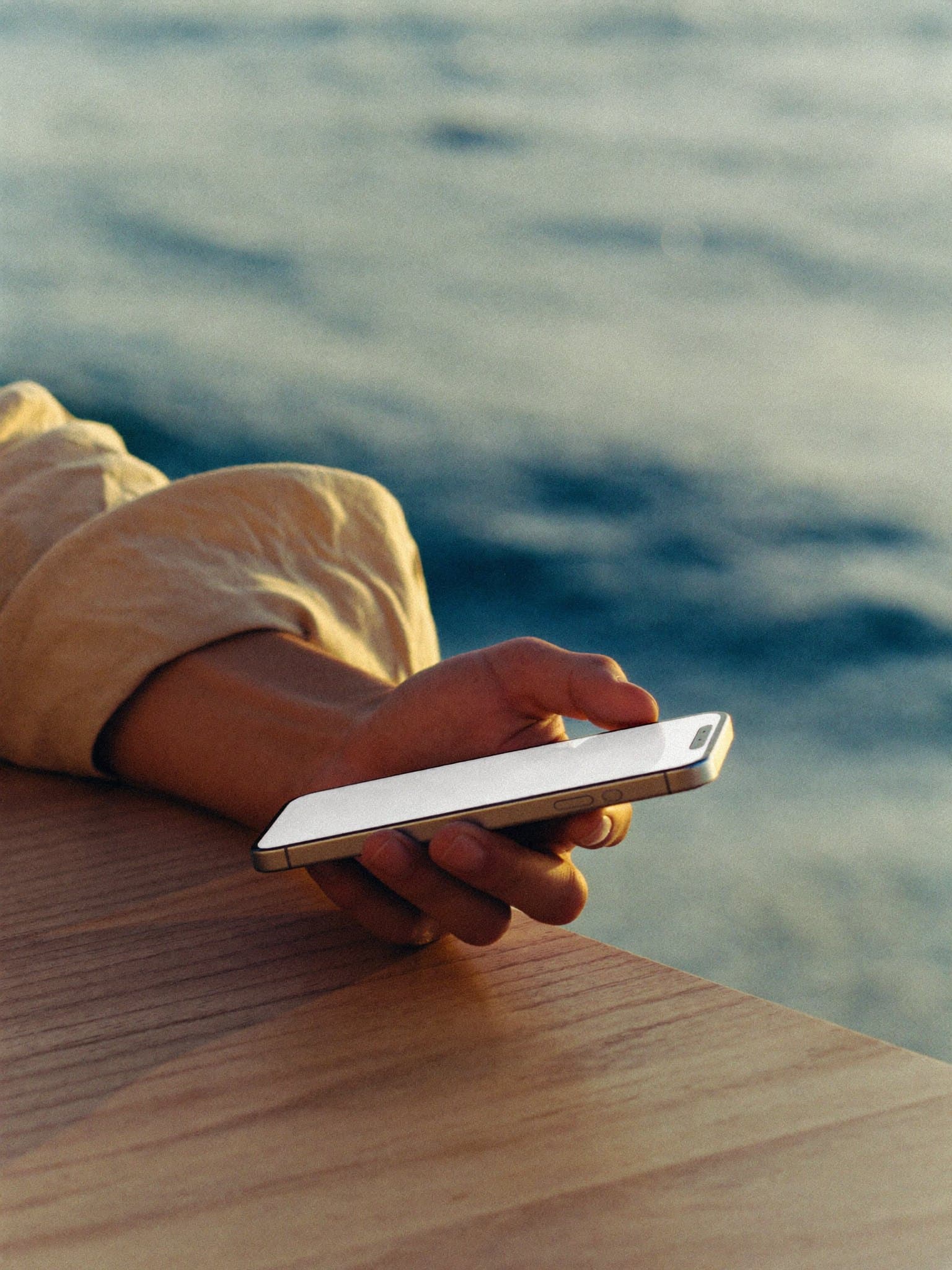 A hand reaching for a phone on a terrace table by the sea
